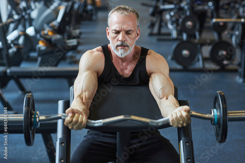 Mature man strengthening arms with barbell in gym