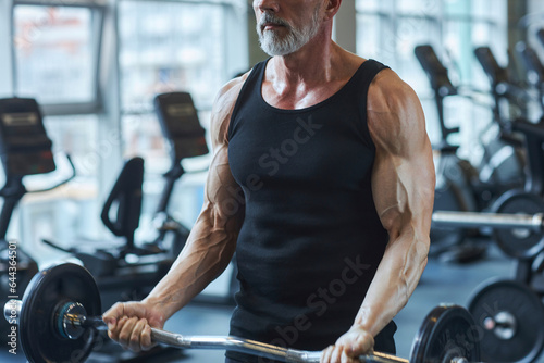 Strong mature man strengthening arms with barbell in gym