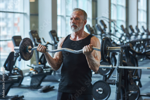 Bearded mature man exercising with barbell in health club