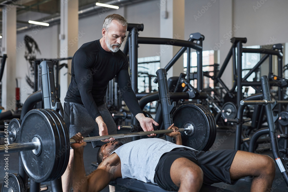 Fitness instructor helping young man with bench press in gym