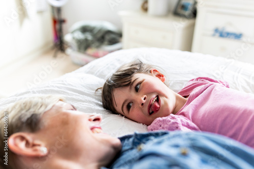 Girl sticking out tongue and lying down by mother in bedroom photo