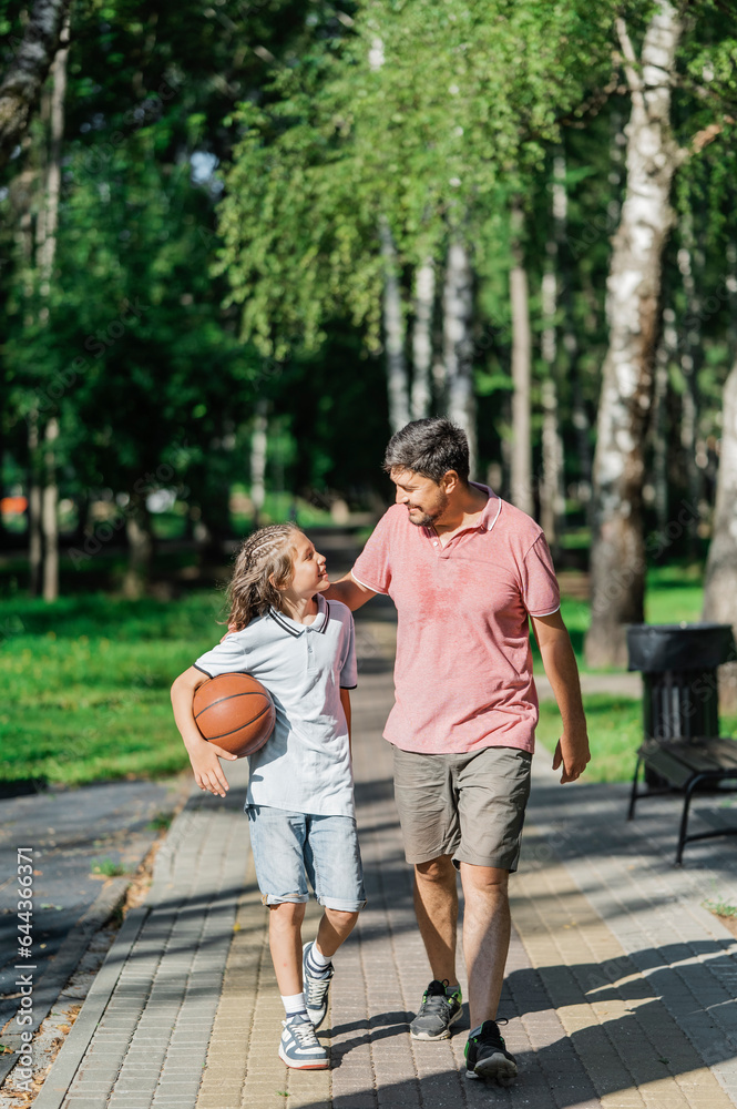 Father talking to son with basketball and walking in park