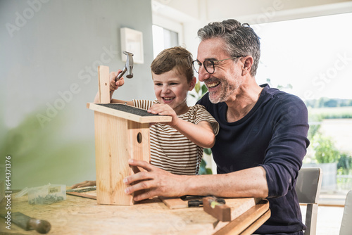 Happy boy timbering birdhouse by grandfather at home photo