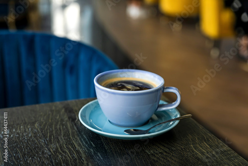 A blue ceramic cup of hot black coffee close-up on a wooden table, atmosphere of a cafe, copy space