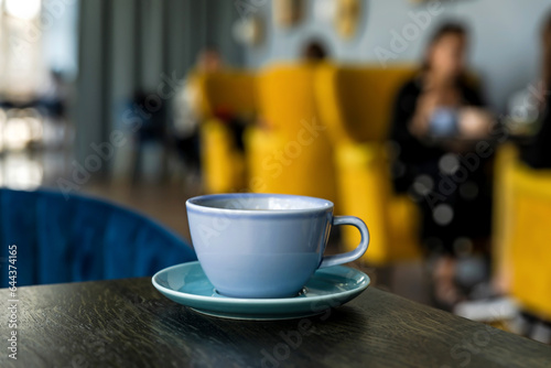 Blue ceramic cup of hot black coffee on wooden table, cafe atmosphere, people in bokeh, copy space