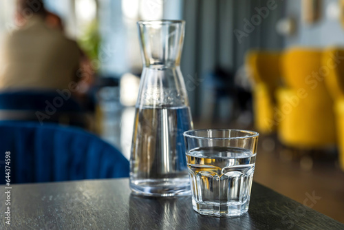 Close-up of glass of water and carafe on table in cafe, coffee shop atmosphere in bokeh background