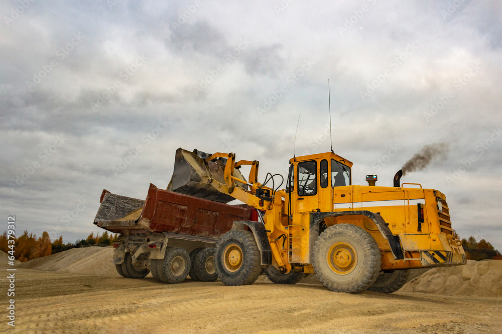 big wheel loader loading stone into truck, tractor loading gravel into truck, big stone mountain with tractor