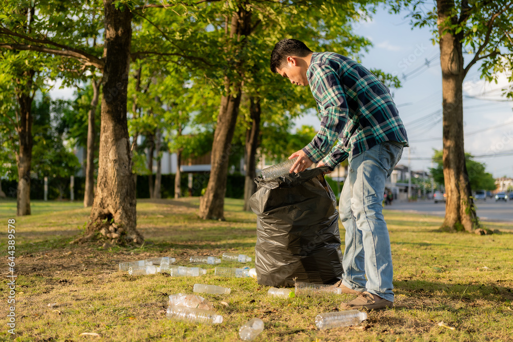 Man's hands collecting garbage, empty plastic water bottles, stew on the floor, dried leaves, young man volunteers collecting plastic bottles in garbage bags, cleaning up, earth ecology day concept