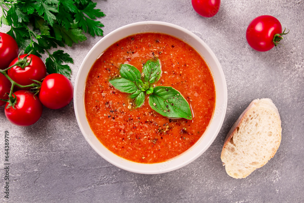 Tomato cream soup with basil and spices on gray background