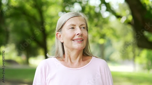 Portrait of senior active gray-haired woman standing in city park looking away. Sporty retired positive female inhales fresh air smiles. Mature old fitness happy runner enjoys being outdoors in nature photo