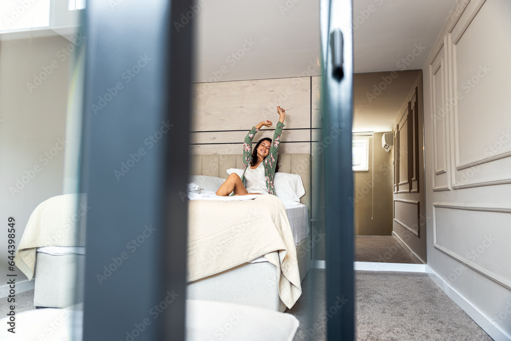 Smiling woman wakes up in the morning, siting on bed in her bedroom and stretching. Smiling woman wakes up in the morning, siting on bed in her bedroom and stretching.