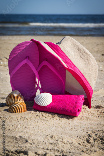 Straw hat, slippers and towel on sand at beach. Accessories for relax in summer