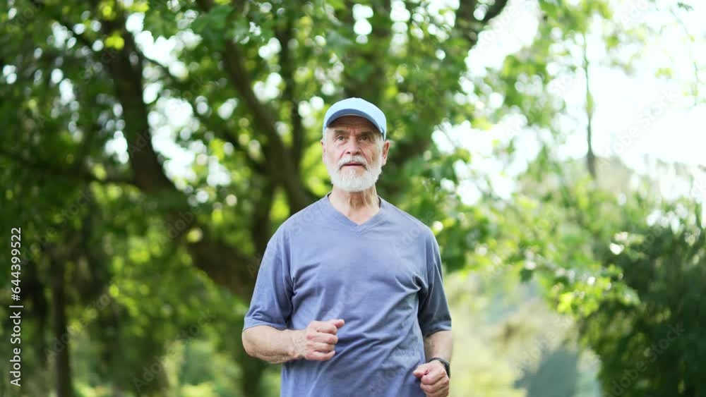 Senior active gray-haired bearded runner jogging in an urban city park. Mature old fitness male in a t-shirt enjoys training outdoors. Elderly sport man on workout outdoors. Concept healthy lifestyle Senior active gray-haired bearded runner jogging in an urban city park. Mature old fitness male in a t-shirt enjoys training outdoors. Elderly sport man on workout outdoors. Concept healthy lifestyle