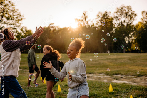 Girl playing amidst bubbles with friends in playground at summer camp