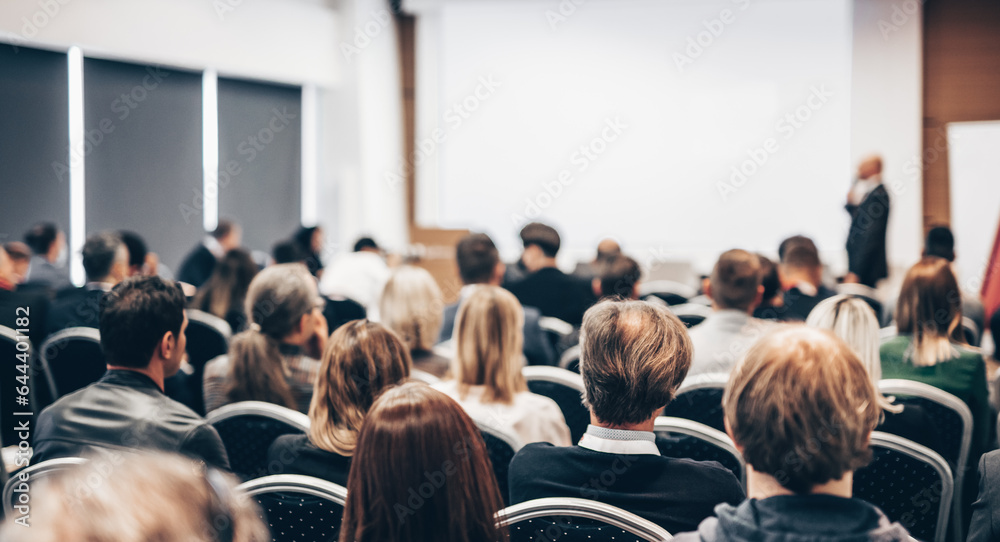 Speaker giving a talk in conference hall at business event. Rear view of unrecognizable people in audience at the conference hall. Business and entrepreneurship concept Speaker giving a talk in conference hall at business event. Rear view of unrecognizable people in audience at the conference hall. Business and entrepreneurship concept