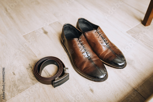 Men's brown leather shoes and a black belt lie on the floor. Close-up photo, top view.