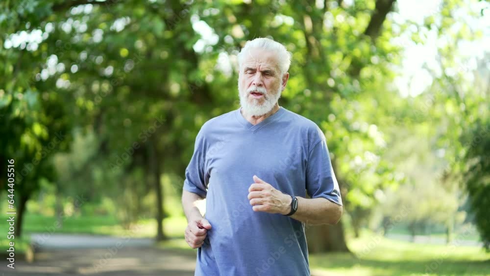 Senior adult active gray haired bearded man has a heart attack while running in an urban city park. Sick mature old male runner suffers from tension in chest. Elderly pensioner has shortness of breath Senior adult active gray haired bearded man has a heart attack while running in an urban city park. Sick mature old male runner suffers from tension in chest. Elderly pensioner has shortness of breath