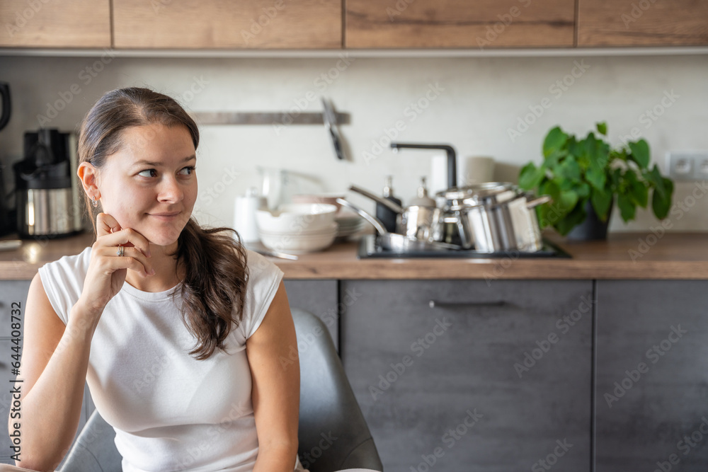 Young happy woman is sitting on background of dirty dishes in the kitchen. Slowdown, self-care, slow life concept Young happy woman is sitting on background of dirty dishes in the kitchen. Slowdown, self-care, slow life concept