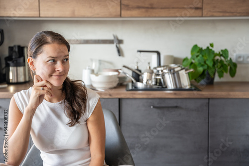 Young happy woman is sitting on background of dirty dishes in the kitchen. Slowdown, self-care, slow life concept