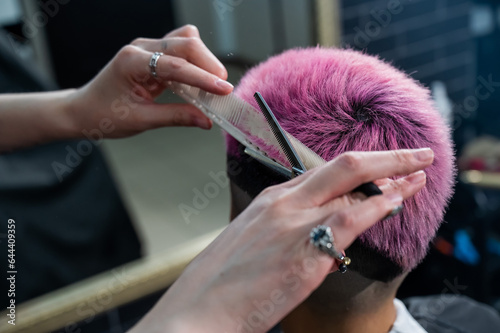 Asian woman with pink hair getting a haircut in a barbershop. 