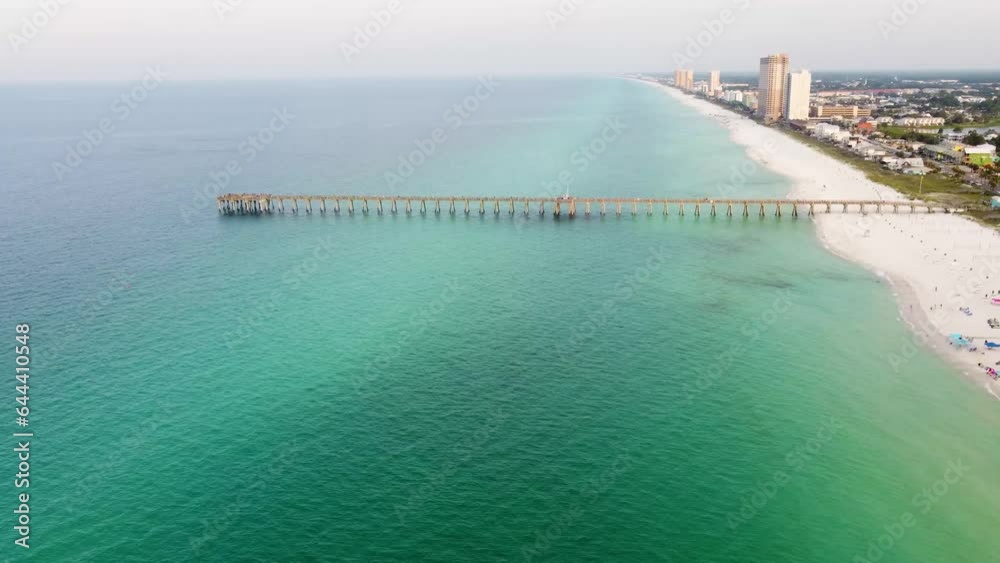 Aerial of Panama City Beach Pier at Pier Park over the gulf of mexico turquoise blue and green water. Aerial shot of the silhouette of a fishing pier on the ocean with a colorful and golden sunrise. Aerial of Panama City Beach Pier at Pier Park over the gulf of mexico turquoise blue and green water. Aerial shot of the silhouette of a fishing pier on the ocean with a colorful and golden sunrise.