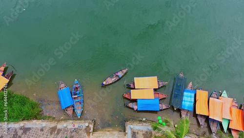 Drone shot with an angle down the river with a boat anchored and a ferryman rowing the boat to take people across the river to go to the market in the ancient town of Hoi An, Vietnam.