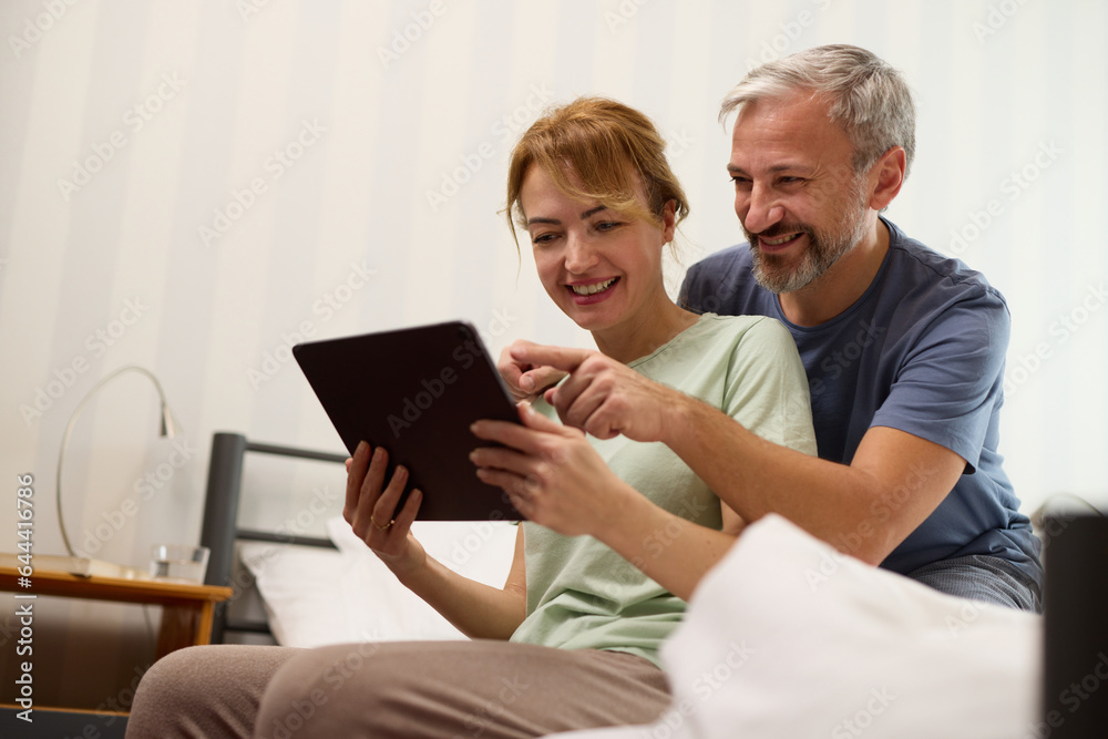 Smiling mature couple using digital tablet at home in bed Smiling mature couple using digital tablet at home in bed