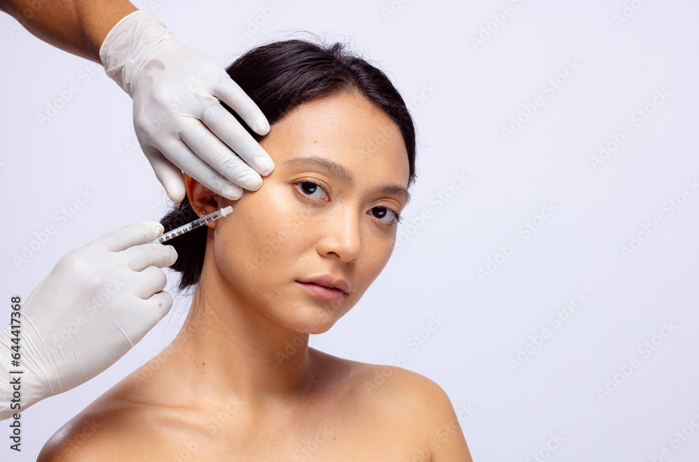 Hands of beautician in white surgical gloves injecting botox in cheek of asian woman, copy space - obrazy, fototapety, plakaty 