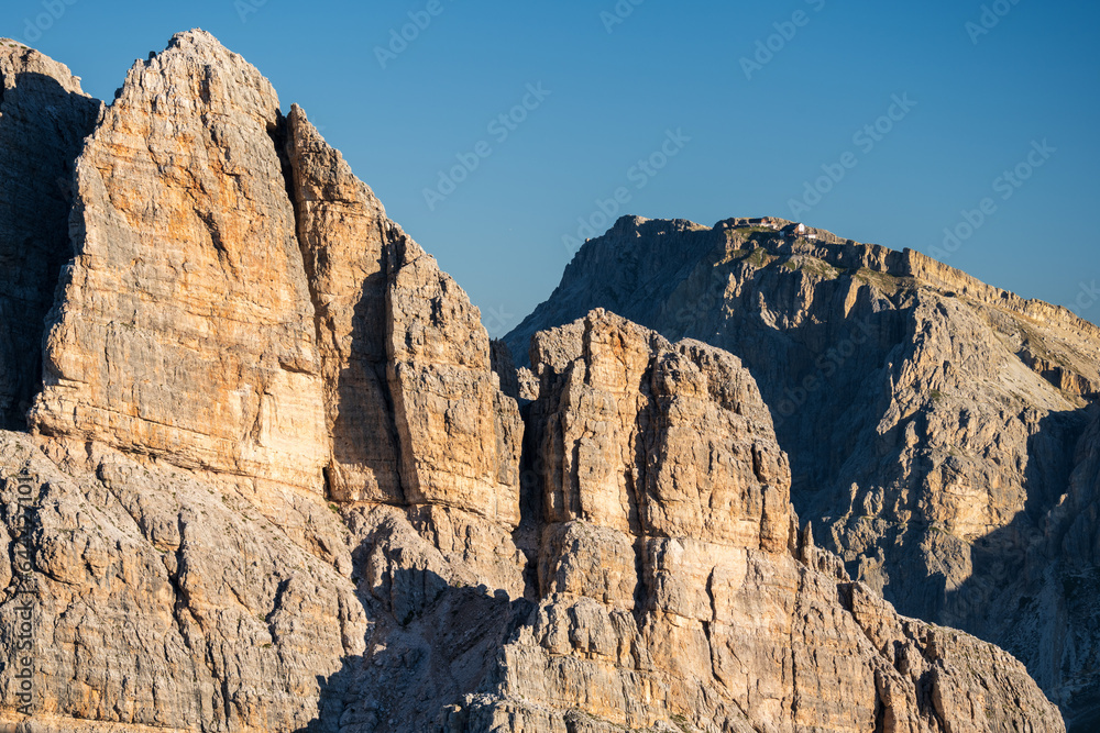Cinque Torri peaks and Tofane Mountains at summer cloudless morning with green grass lighteen by warm light of sun