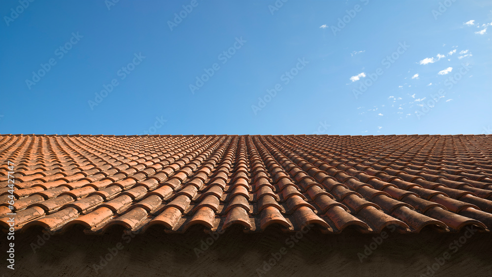 Weathered red tile roof with side sunlight on a blue sky background Weathered red tile roof with side sunlight on a blue sky background