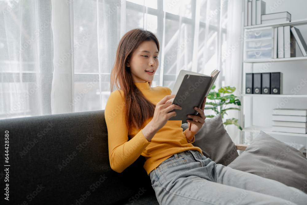 Asian woman in the living room and reading a book, female company employee on vacation, using vacation time and free time to relax at home, weekend vacation doing activities. Asian woman in the living room and reading a book, female company employee on vacation, using vacation time and free time to relax at home, weekend vacation doing activities.