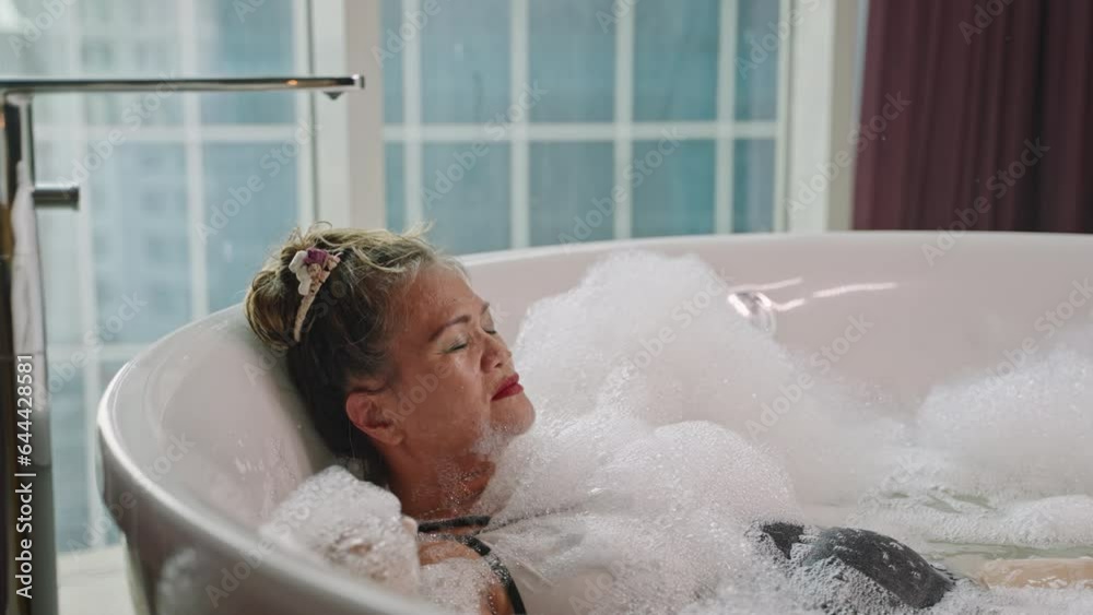 Asian senior woman relaxing in warm bubble bath. Elderly female enjoys