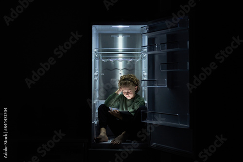 Focused kid watching movie on tablet while sitting in fridge