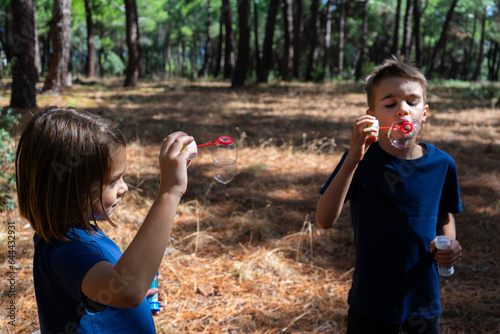 Two children playing with soap bubbles in the forest