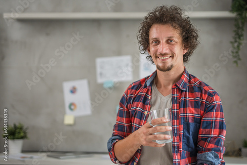 One young man standing in the office  holding a glass with water looking at camera, business and lifestyle concept