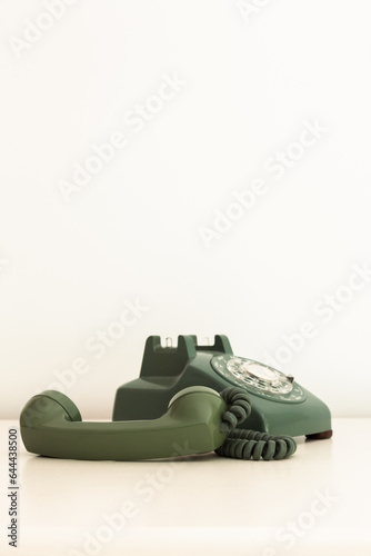 Vertical view of vintage olive green rotary phone with receiver unhooked set on pale background