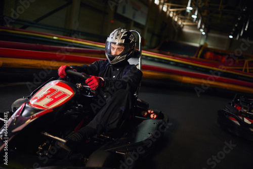 focused speed racer in helmet driving go kart car on indoor circuit, motorsport competition concept