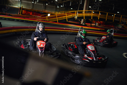 diverse men driving go kart near checkered black and white racing flag on blurred foreground