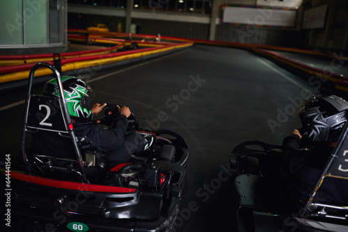 two multicultural men in helmets and sportswear driving go kart on indoor circuit, competitors © LIGHTFIELD STUDIOS