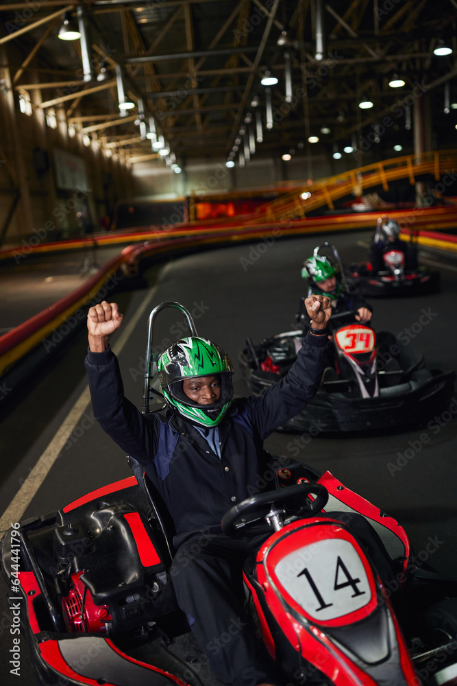 excited african american go cart driver in helmet raising hands and winning race on circuit, go-kart