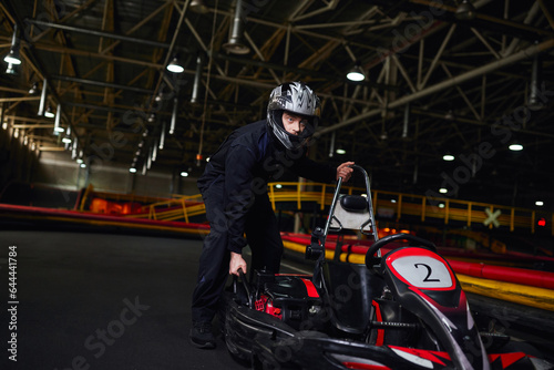 motorsport and speed drive, focused kart driver in sportswear and helmet pushing go kart on circuit