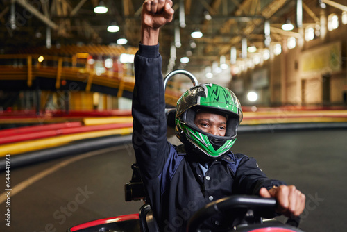 Go kart speed drive indoor race, excited african american driver in helmet celebrating victory