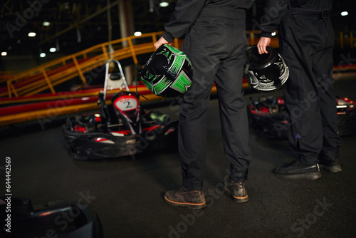 cropped view of two kart racers standing near racing cars and holding helmets, go-kart drivers © LIGHTFIELD STUDIOS