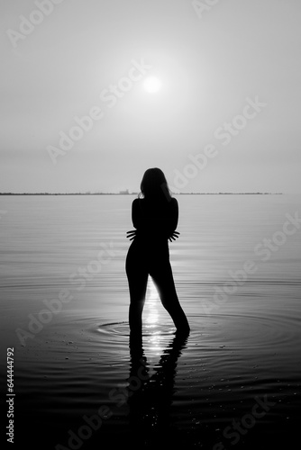 Woman's silhouette in the sea in the backlight of the sun. Black and white photo of a girl in sea water in front of the sun.
