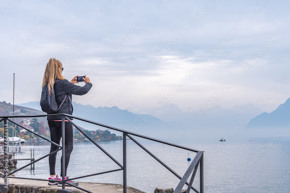 Woman holding mobile phone while photographing lake and mountain landscape. Woman holding mobile phone while photographing lake and mountain landscape.