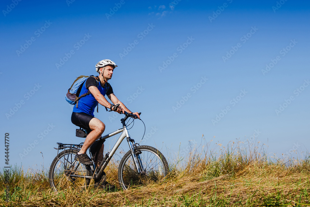 Young man cycling on a rural road through green meadow Young man cycling on a rural road through green meadow