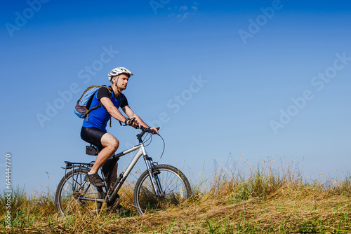 Young man cycling on a rural road through green meadow