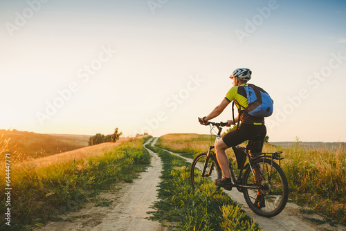 Young man cycling on a rural road through sunset summer meadow