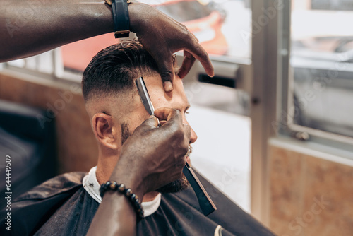 Crop barber shaving hair of client with razor photo