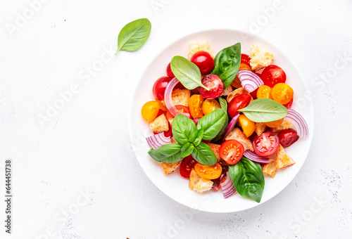 Panzanella salad with stale ciabatta bread, colorful tomatoes, red onion, olive oil, salt and green basil, white table background, top view